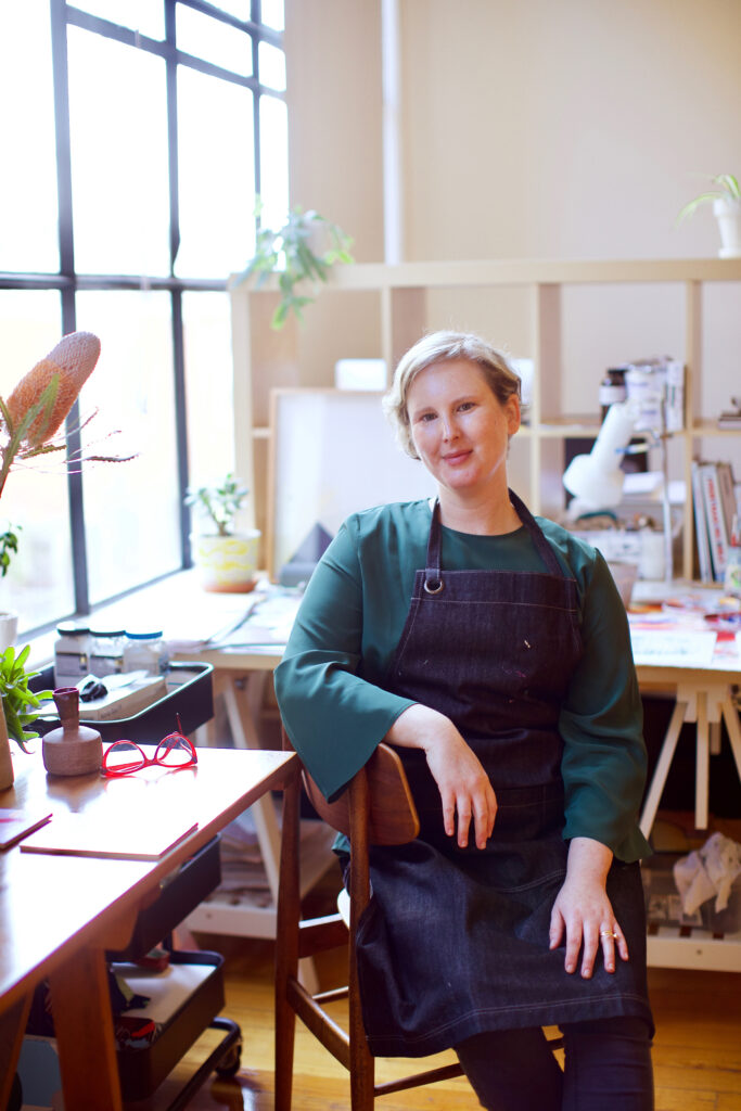 A woman artist sitting in a studio next to a window with bright light.