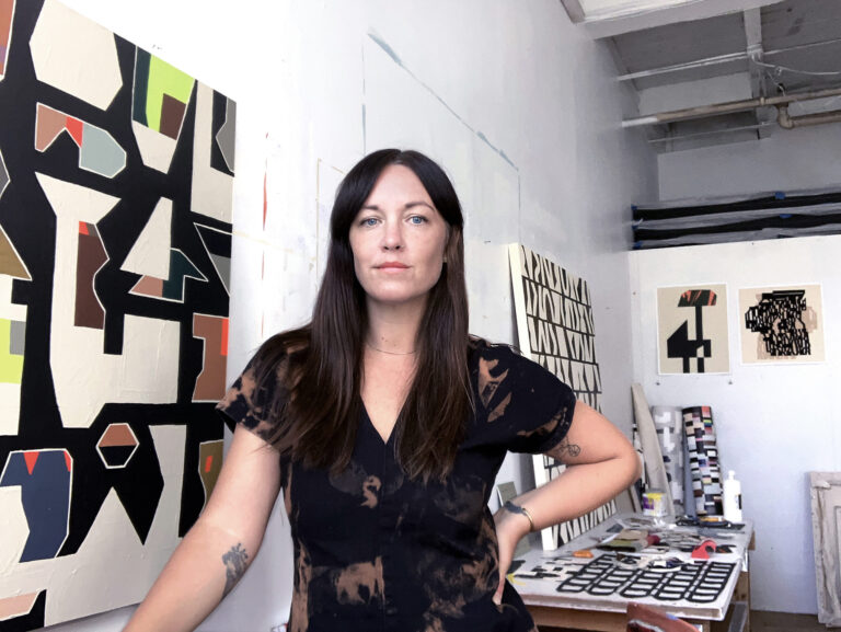 A photo of a woman wearing black and standing in her art studio.